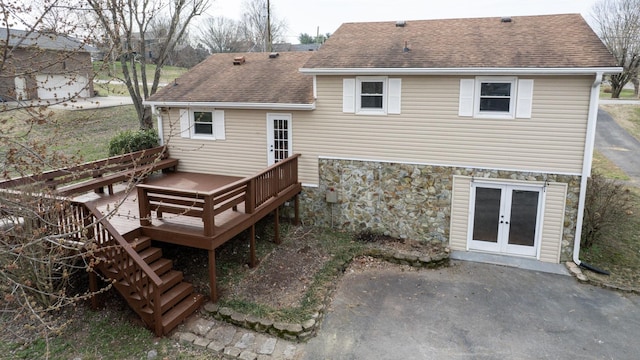 back of house with stone siding, french doors, a wooden deck, and roof with shingles