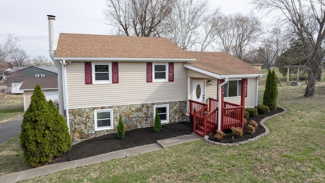 tri-level home with a front lawn, a garage, stone siding, and a shingled roof