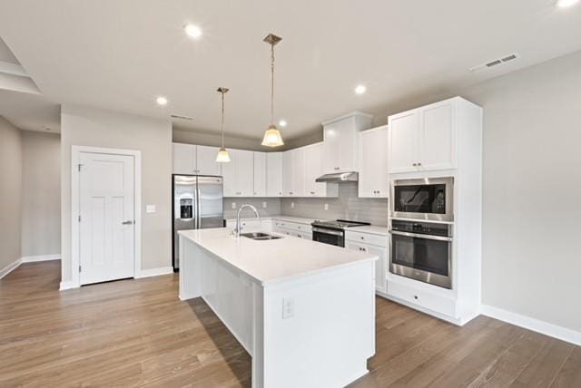 kitchen featuring an island with sink, decorative backsplash, white cabinets, stainless steel appliances, and a sink