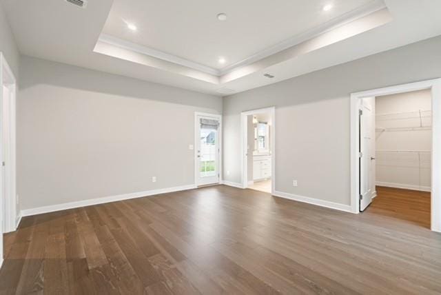 unfurnished bedroom featuring a tray ceiling, wood finished floors, baseboards, and ornamental molding