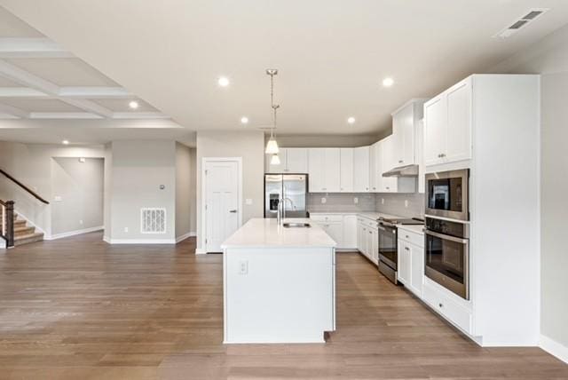 kitchen with a kitchen island with sink, a sink, decorative backsplash, light wood-style floors, and appliances with stainless steel finishes