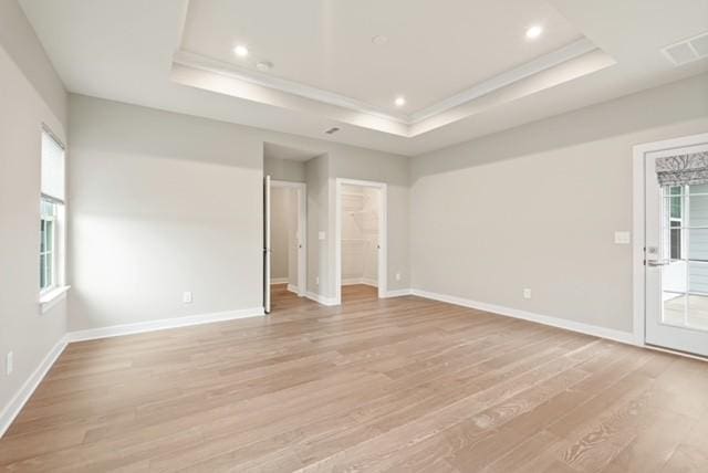 unfurnished room with visible vents, a tray ceiling, light wood-style floors, crown molding, and baseboards