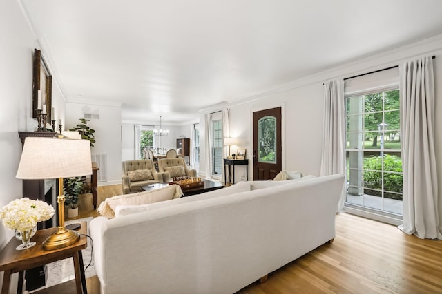 living room with a notable chandelier, visible vents, light wood-type flooring, and ornamental molding