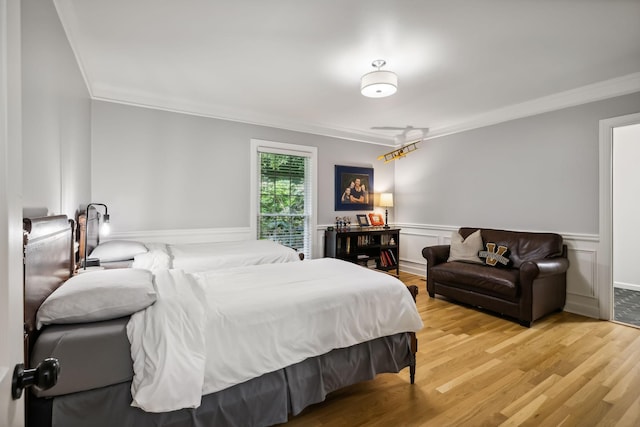 bedroom featuring light wood-type flooring, a wainscoted wall, and ornamental molding