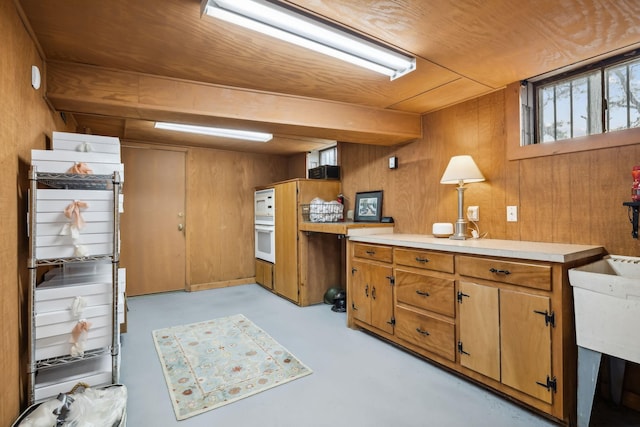 kitchen with oven, concrete floors, wood walls, brown cabinetry, and light countertops