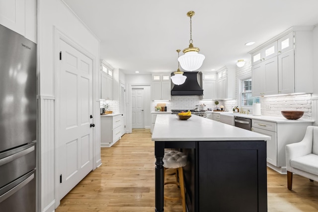 kitchen with premium range hood, light wood-type flooring, a breakfast bar, appliances with stainless steel finishes, and white cabinets