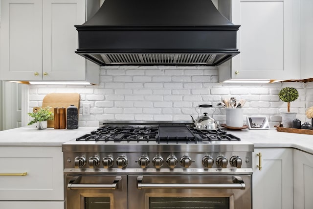 kitchen with double oven range, backsplash, white cabinets, and custom range hood