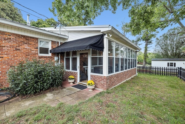 doorway to property featuring brick siding, a lawn, and fence