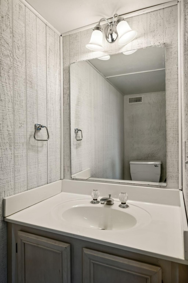 half bath with vanity, toilet, and visible vents