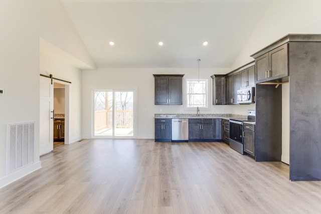 kitchen featuring visible vents, a barn door, light wood-style flooring, stainless steel appliances, and a sink