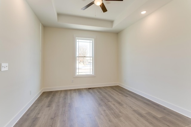 spare room featuring ceiling fan, a raised ceiling, baseboards, and wood finished floors