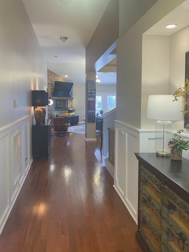 corridor with visible vents, an upstairs landing, dark wood-type flooring, a wainscoted wall, and lofted ceiling