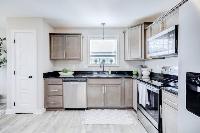 kitchen with light wood finished floors, dark stone counters, hanging light fixtures, stainless steel appliances, and a sink