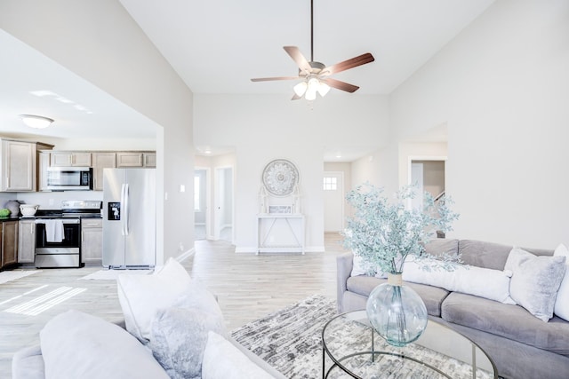 living area with baseboards, light wood-style floors, lofted ceiling, and ceiling fan