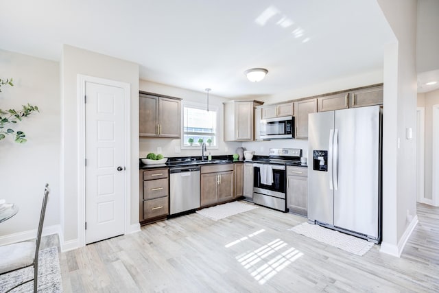 kitchen featuring dark countertops, light wood finished floors, pendant lighting, appliances with stainless steel finishes, and a sink