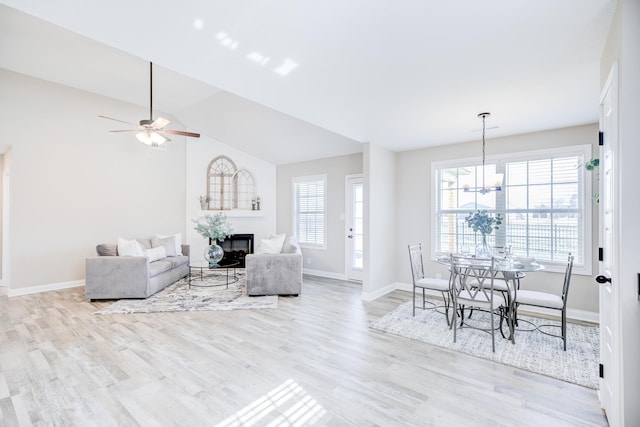 living area with light wood finished floors, a glass covered fireplace, baseboards, and lofted ceiling