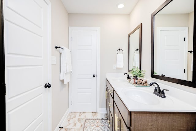 full bath with double vanity, marble finish floor, baseboards, and a sink