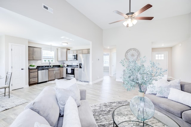 living room with visible vents, baseboards, ceiling fan, and light wood finished floors