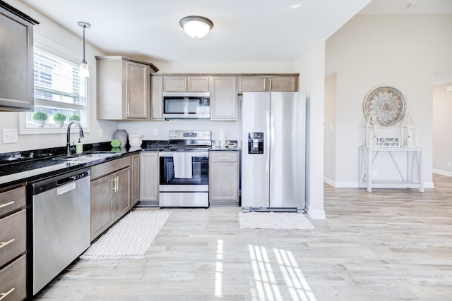 kitchen featuring light wood-style flooring, a sink, decorative light fixtures, stainless steel appliances, and baseboards