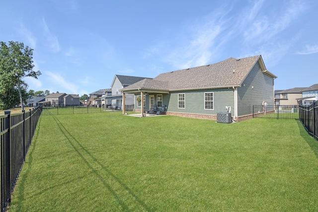 back of property with a yard, a fenced backyard, a shingled roof, a patio area, and a residential view