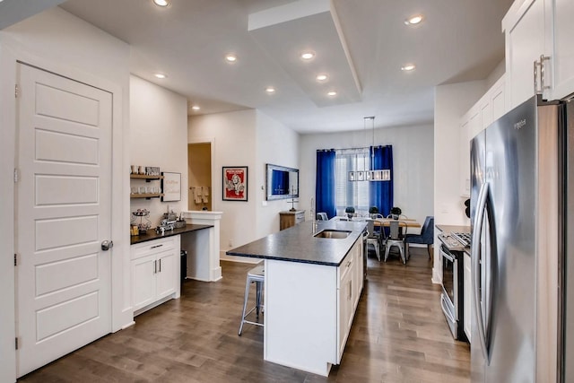 kitchen with a center island with sink, dark wood-type flooring, appliances with stainless steel finishes, white cabinetry, and dark countertops