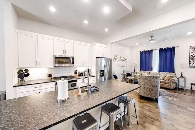 kitchen with light wood-type flooring, a kitchen bar, recessed lighting, stainless steel appliances, and white cabinets