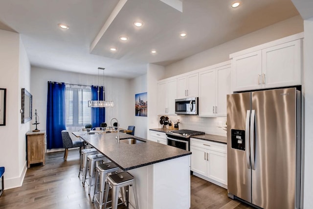 kitchen featuring an island with sink, a sink, dark countertops, white cabinetry, and stainless steel appliances