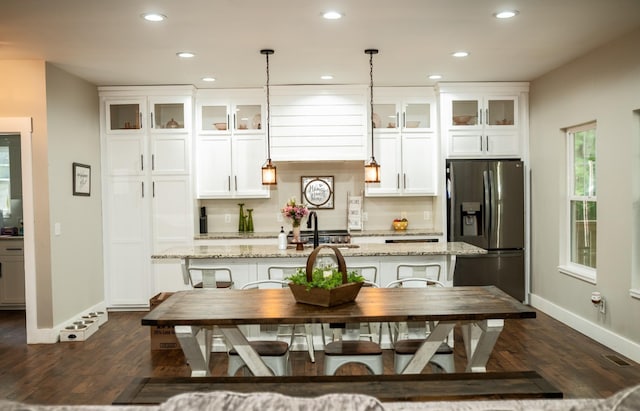 kitchen featuring decorative backsplash, a kitchen island with sink, stainless steel refrigerator with ice dispenser, and white cabinetry