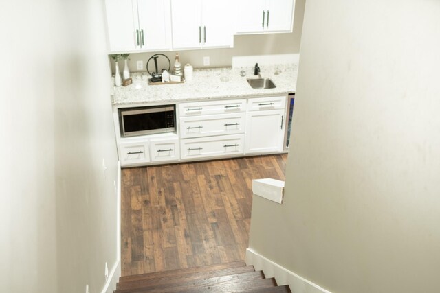 bar with dark wood-style flooring, a sink, stainless steel microwave, baseboards, and stairs