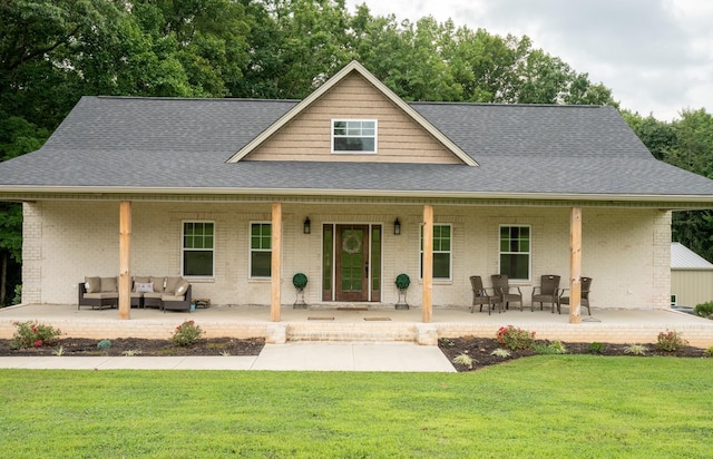 farmhouse-style home with a front yard, roof with shingles, covered porch, brick siding, and an outdoor hangout area