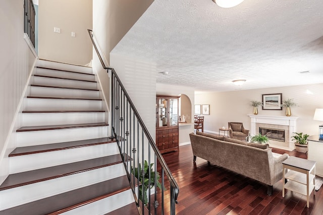 stairway featuring a textured ceiling, wood finished floors, arched walkways, a premium fireplace, and baseboards