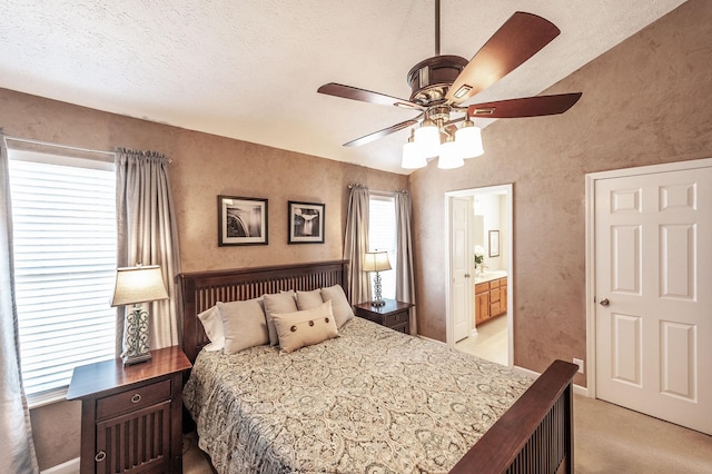 bedroom featuring light carpet, ensuite bathroom, a textured wall, a textured ceiling, and a ceiling fan