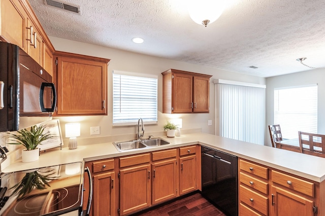 kitchen featuring visible vents, a sink, a peninsula, dishwasher, and dark wood-style flooring