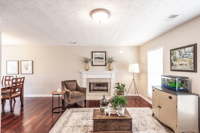 living room with a premium fireplace, visible vents, baseboards, and dark wood-style flooring