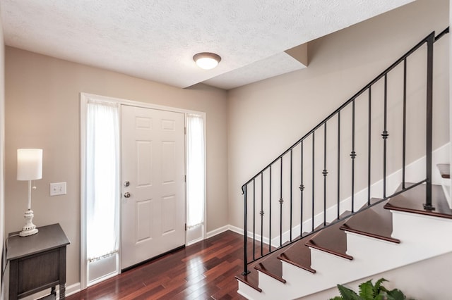 foyer entrance featuring stairway, baseboards, a textured ceiling, and dark wood finished floors