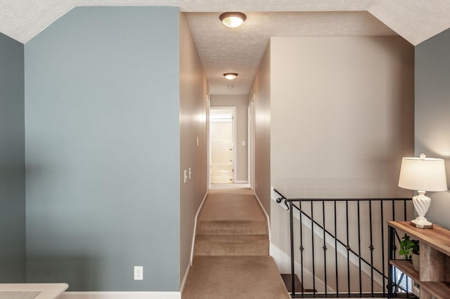 hall featuring a textured ceiling, baseboards, and carpet floors