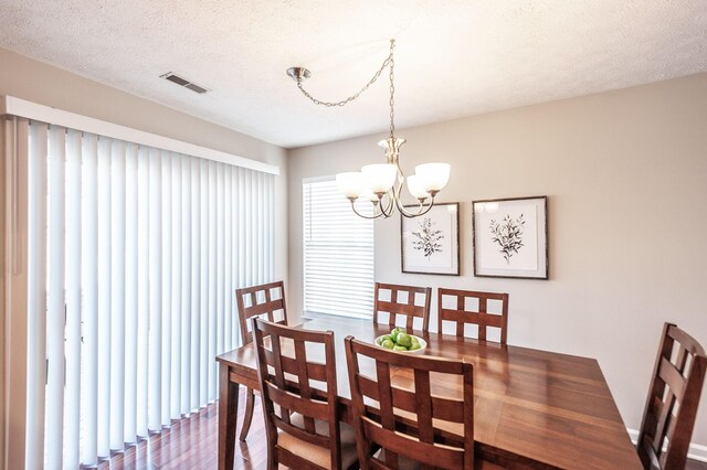 dining room featuring an inviting chandelier, wood finished floors, visible vents, and a textured ceiling