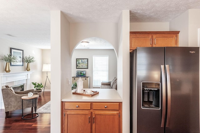 kitchen featuring brown cabinetry, light countertops, a fireplace, dark wood-style floors, and stainless steel fridge