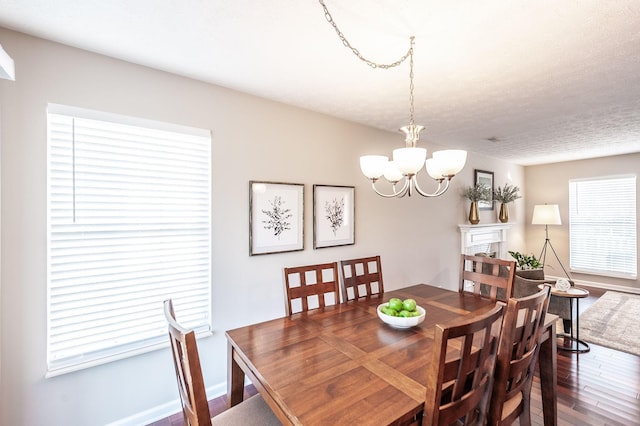 dining space featuring wood finished floors, baseboards, an inviting chandelier, a fireplace, and a textured ceiling