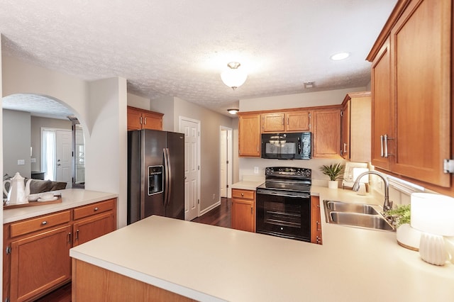 kitchen featuring black appliances, a sink, arched walkways, a peninsula, and light countertops