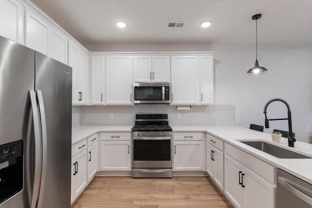 kitchen with visible vents, a sink, appliances with stainless steel finishes, white cabinets, and light wood finished floors