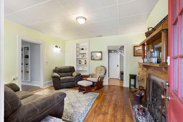 living area with built in features, wood finished floors, visible vents, baseboards, and a fireplace