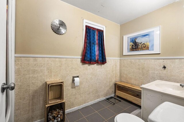 half bath featuring toilet, wainscoting, tile patterned floors, tile walls, and a sink