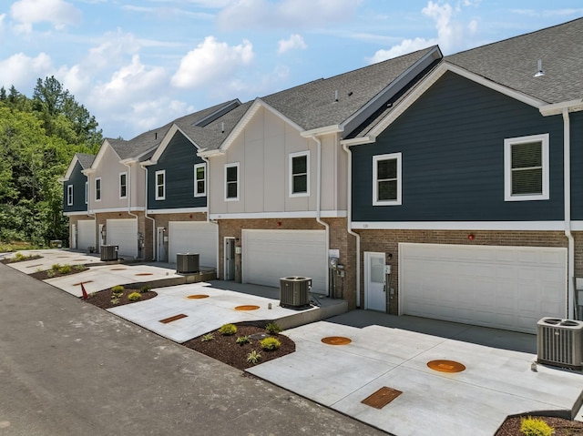 view of property featuring central air condition unit, brick siding, board and batten siding, and concrete driveway