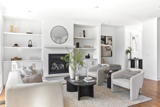 living room with ornamental molding, built in features, a glass covered fireplace, wood finished floors, and baseboards