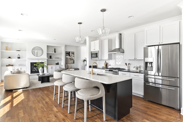 kitchen with dark wood-type flooring, wall chimney range hood, appliances with stainless steel finishes, and a sink