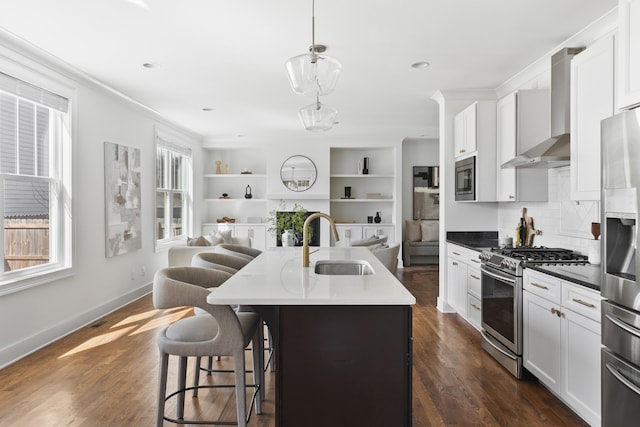 kitchen featuring wall chimney range hood, dark wood finished floors, open floor plan, appliances with stainless steel finishes, and a sink