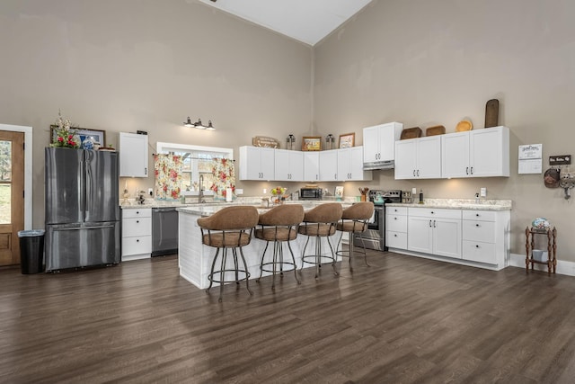 kitchen featuring high vaulted ceiling, white cabinets, appliances with stainless steel finishes, a kitchen breakfast bar, and a center island