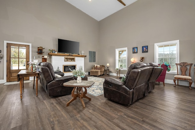 living room with a glass covered fireplace, dark wood-style floors, baseboards, and high vaulted ceiling