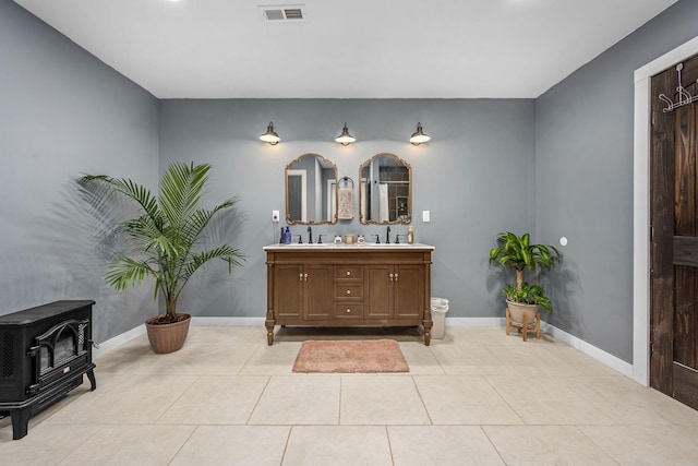 full bath with tile patterned floors, visible vents, double vanity, baseboards, and a wood stove